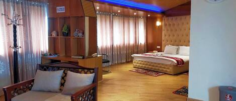 A hotel room with a bed, a sofa, a desk, a chair, a clock, and a trash bin.