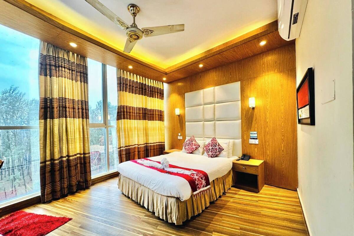 Un dormitorio moderno con una cama grande, un ventilador de techo, una mesita de noche y vistas amplias a través de grandes ventanales.