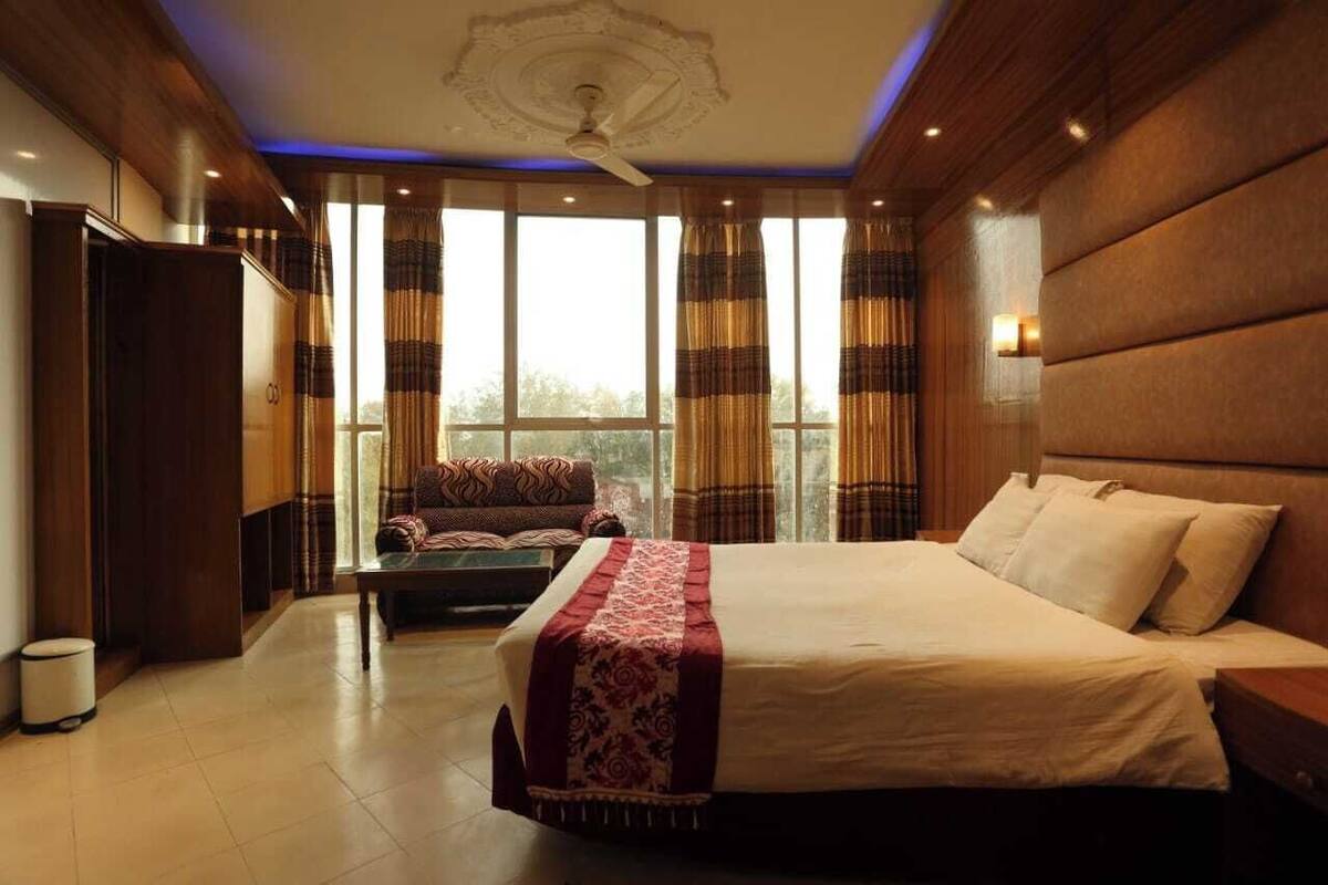 Un dormitorio con cama, sofá, ventilador de techo y ventanas grandes con cortinas.