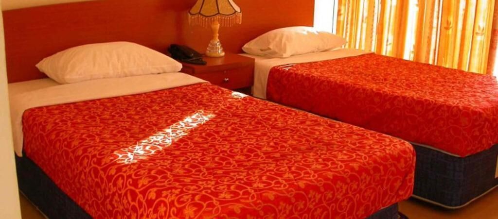 Hotelkamer met twee bedden, elk met een rood bedlaken met patroon, een nachtkastje met lamp en een telefoon.