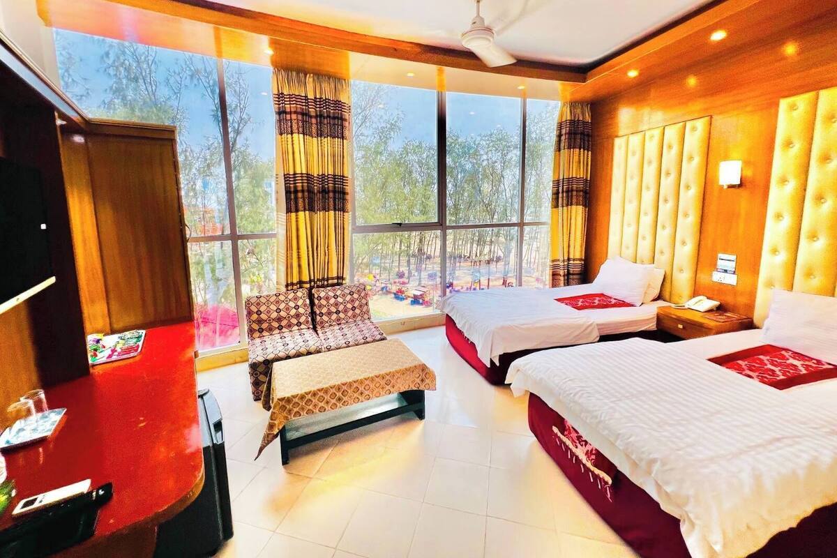 Una habitación de hotel con dos camas, un escritorio, una silla y ventanas amplias.