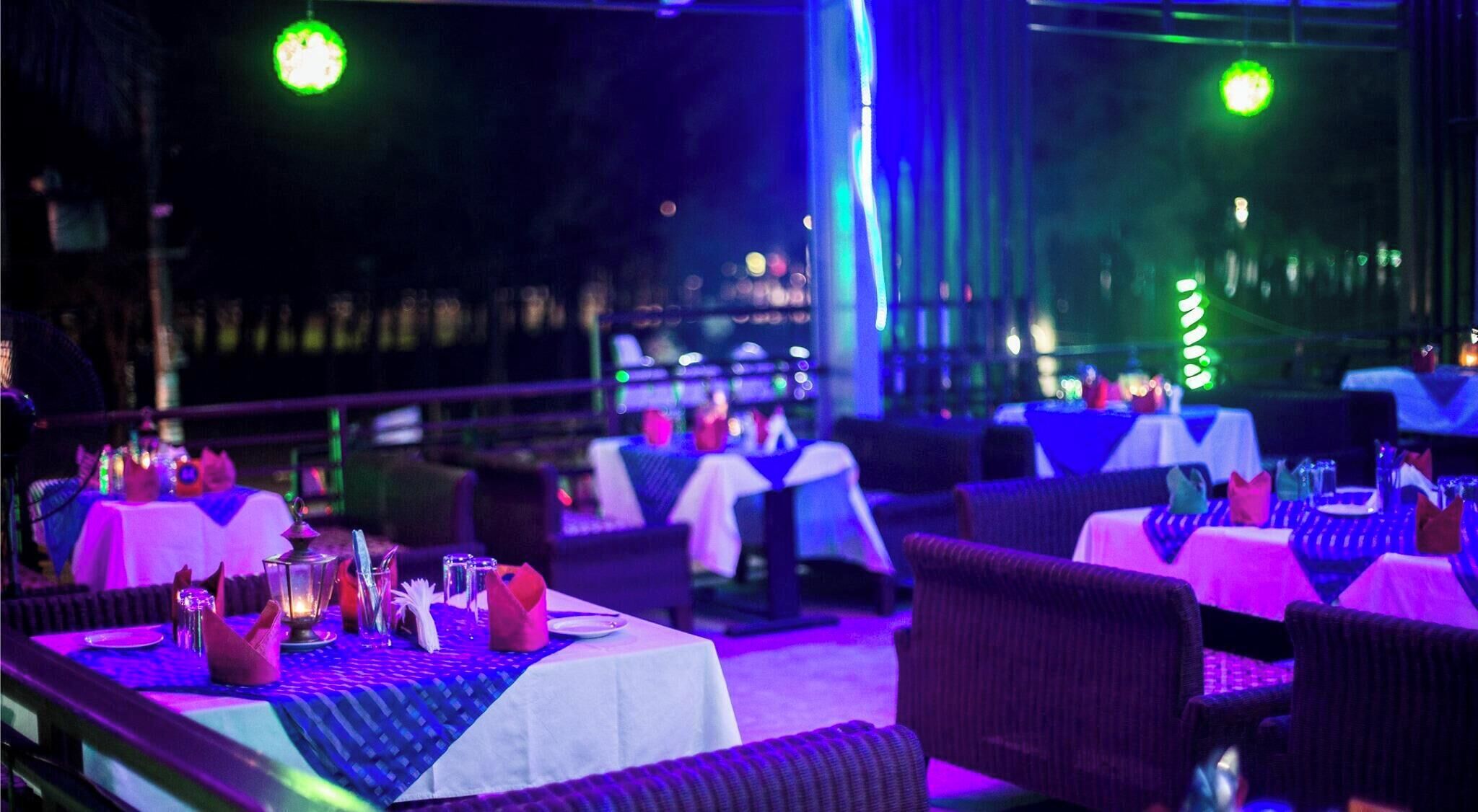 An outdoor dining area with tables set for a meal, chairs, and a view of the cityscape in the background.