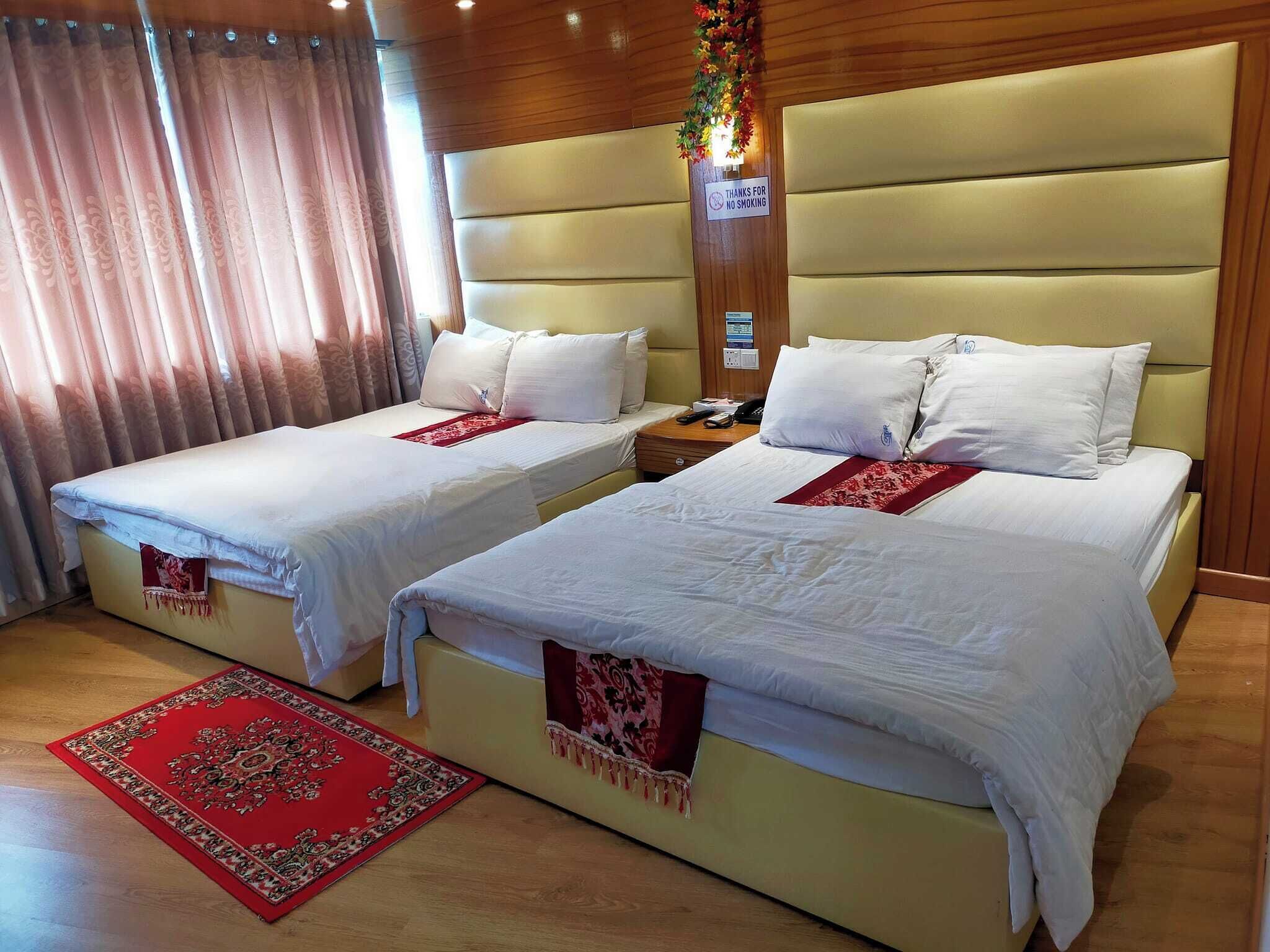 A hotel room with two beds, a red rug, and a sign indicating no smoking.