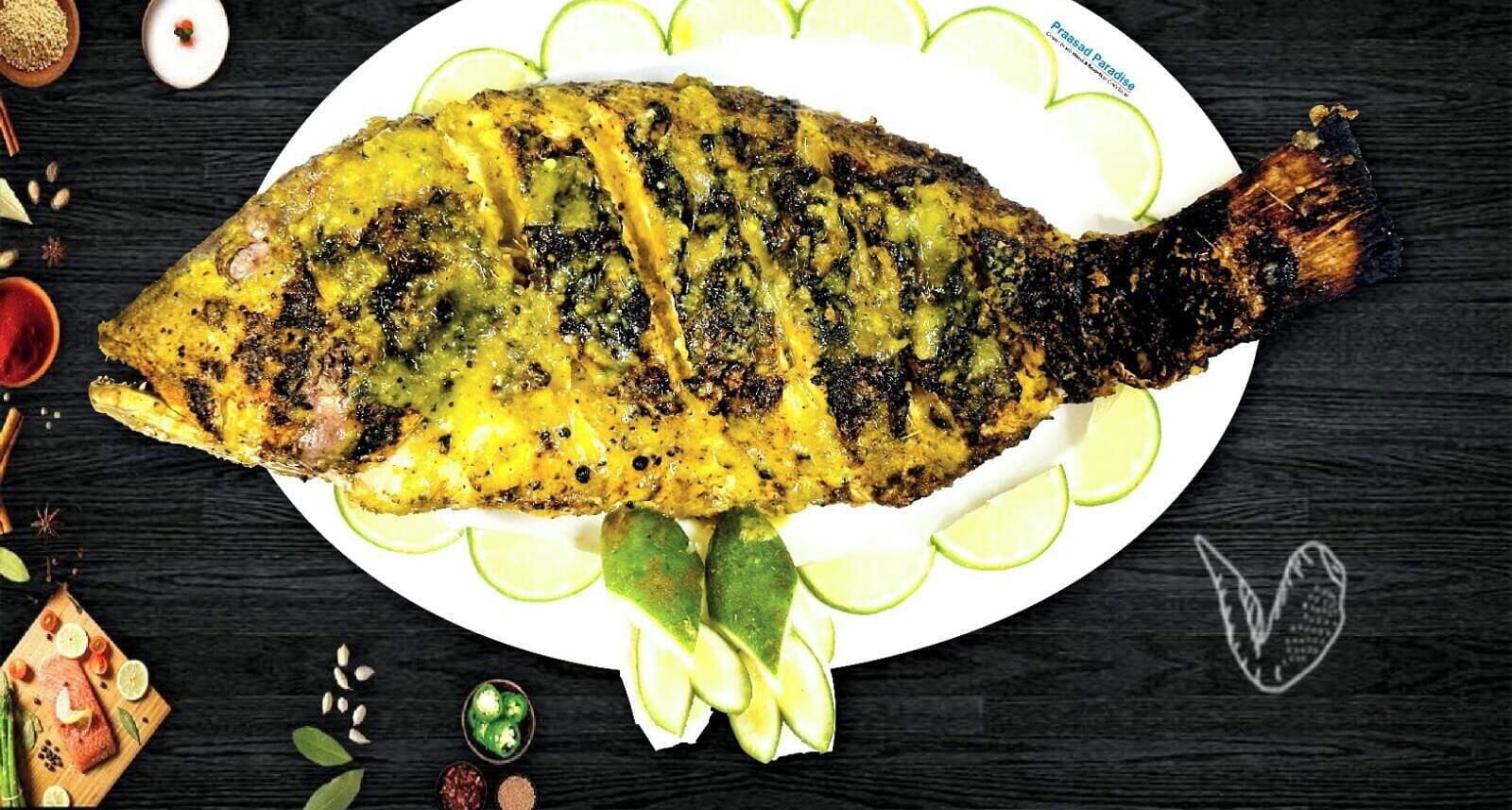 A whole grilled fish on a plate with lime slices and herbs.