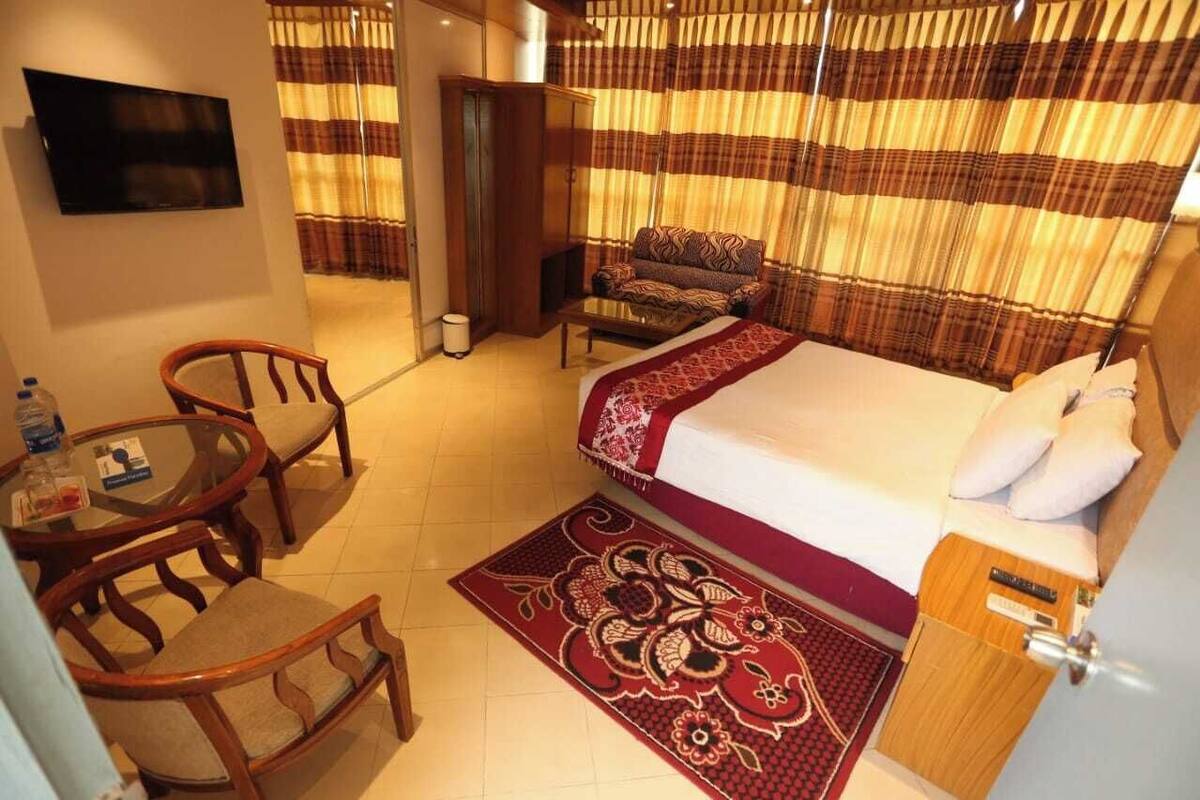 Una habitación de hotel con cama, sofá, televisor, una mesita con sillas y un tapete estampado.