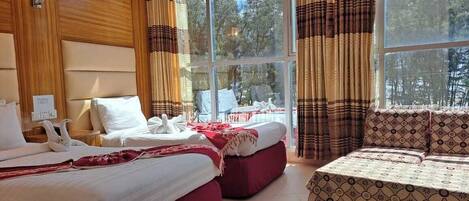 A hotel room with two beds, a sofa, a large window with curtains, and a view of trees.