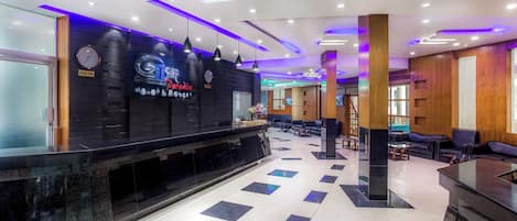 A hotel lobby with a reception desk, seating area, and a clock on the wall.