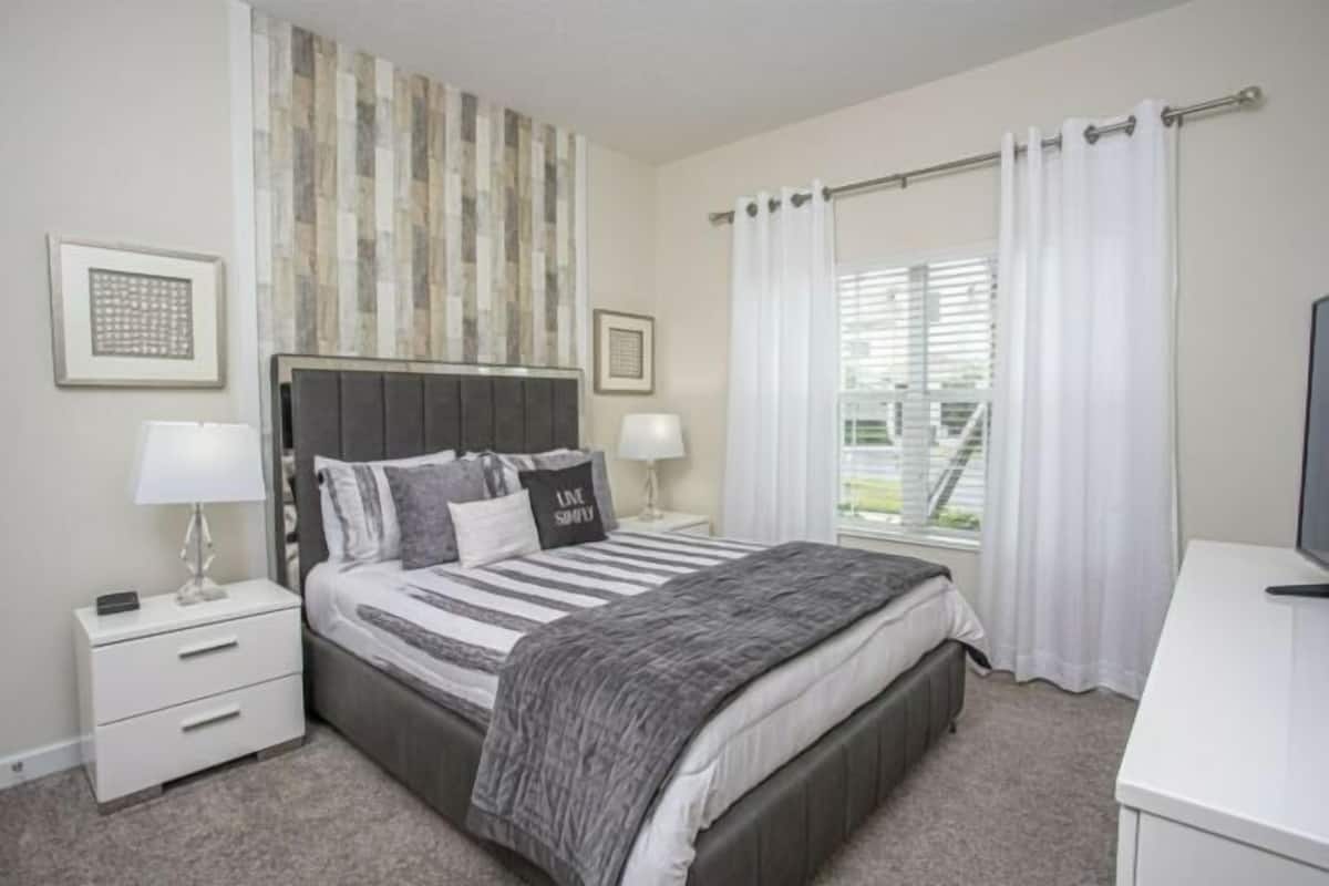 A bedroom with a bed, nightstands, a desk, and a window with curtains.