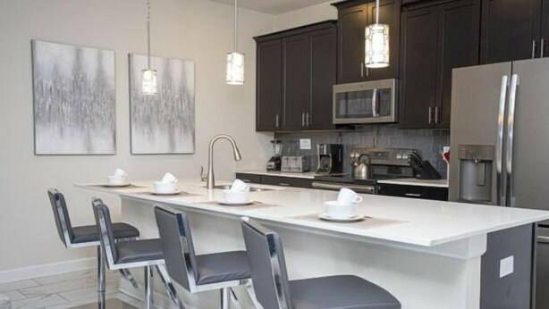 Una cocina moderna con armarios oscuros, electrodomésticos de acero inoxidable y una isla central con taburetes de bar.