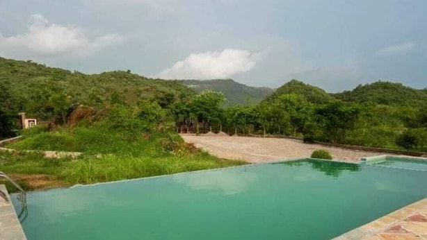Una piscina con borde de piedra, rodeada de follaje y colinas al fondo.