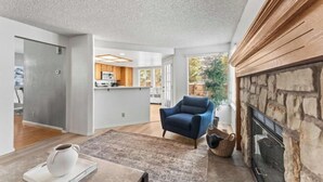 Una sala de estar moderna con chimenea, un sillón azul y una cocina al fondo.