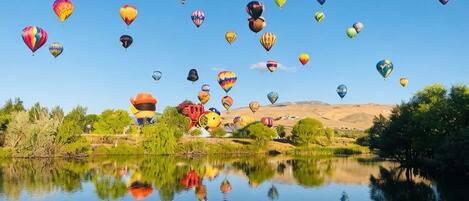 A calm lake with reflections of hot air balloons and a clear sky.
