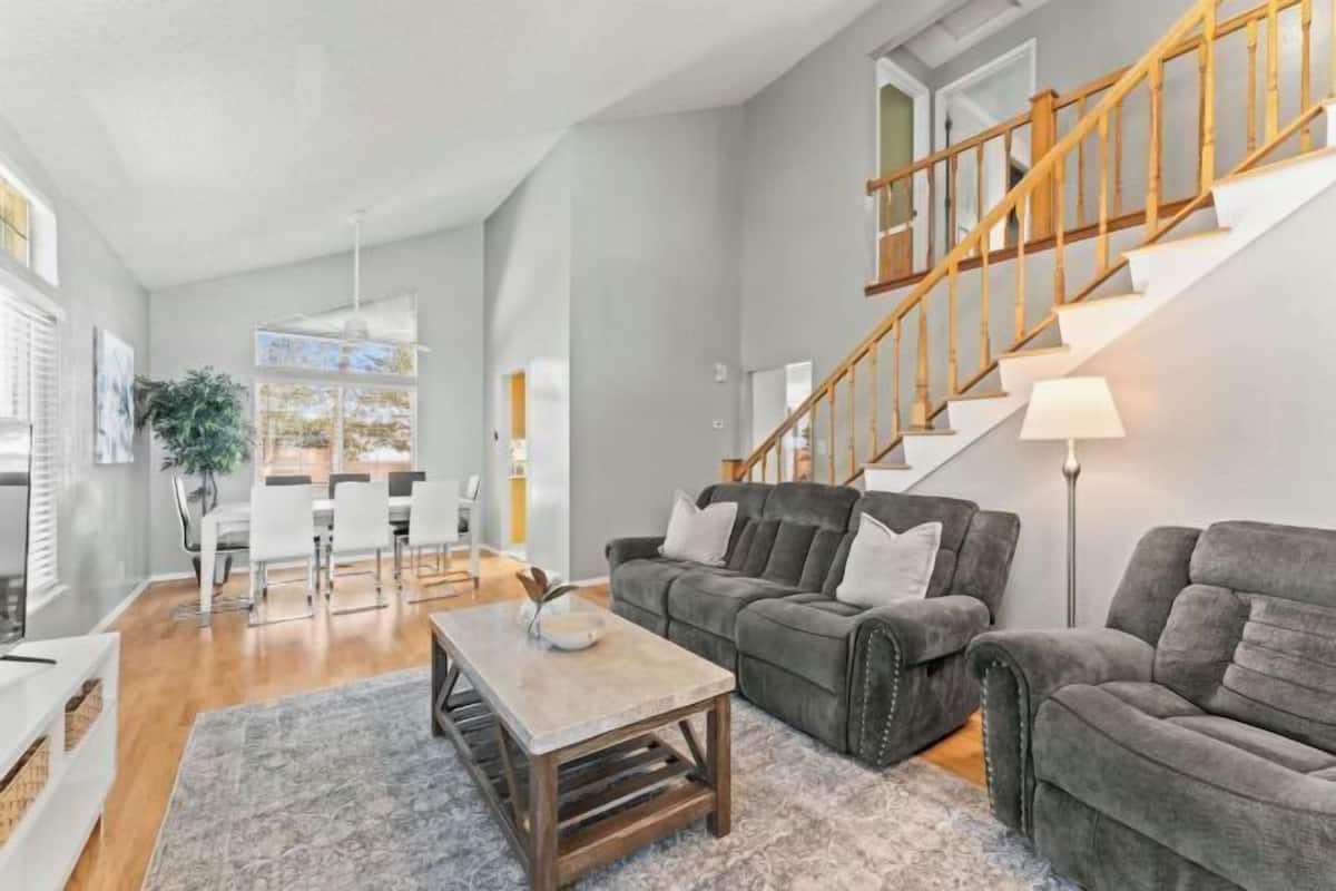 A spacious living room with a staircase, a dining area, and a kitchen in the background.
