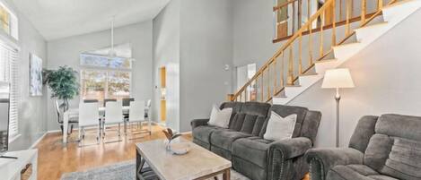 A spacious living room with a staircase, a dining area, and a kitchen in the background.