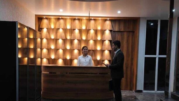 A reception desk with a wooden panel backdrop and a modern ceiling design. - Xenious Opulent Hamirpur (Barsar)