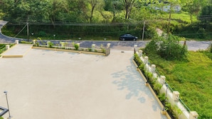 An empty parking lot with a paved surface, surrounded by greenery and a road. - Xenious Opulent Hamirpur (Barsar)
