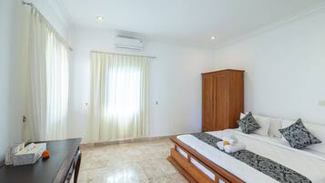 A hotel room with a bed, a wooden wardrobe, a desk with a tissue box and a flower, and a window with curtains.