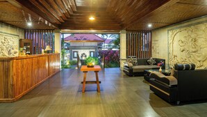 A reception area with a wooden reception desk, a seating area with sofas, and a view of the outside. - Awatara Villas and Resort Ubud (Kemenuh)