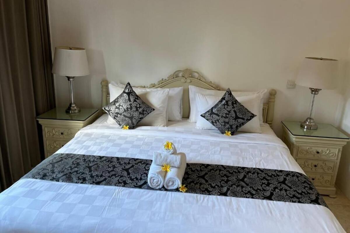A neatly made bed with white and black patterned linens, two decorative pillows, and a set of towels with yellow flowers.