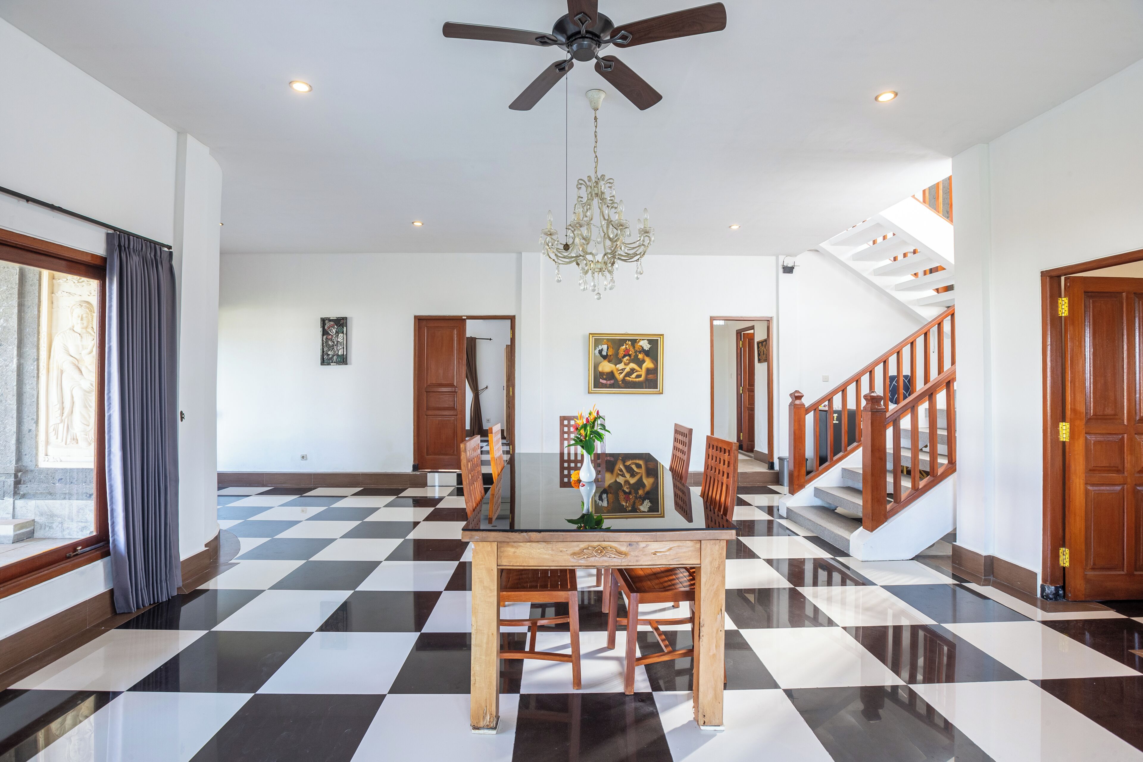 A spacious room with a checkered floor, a dining table with chairs, a chandelier, and a staircase leading to another level.