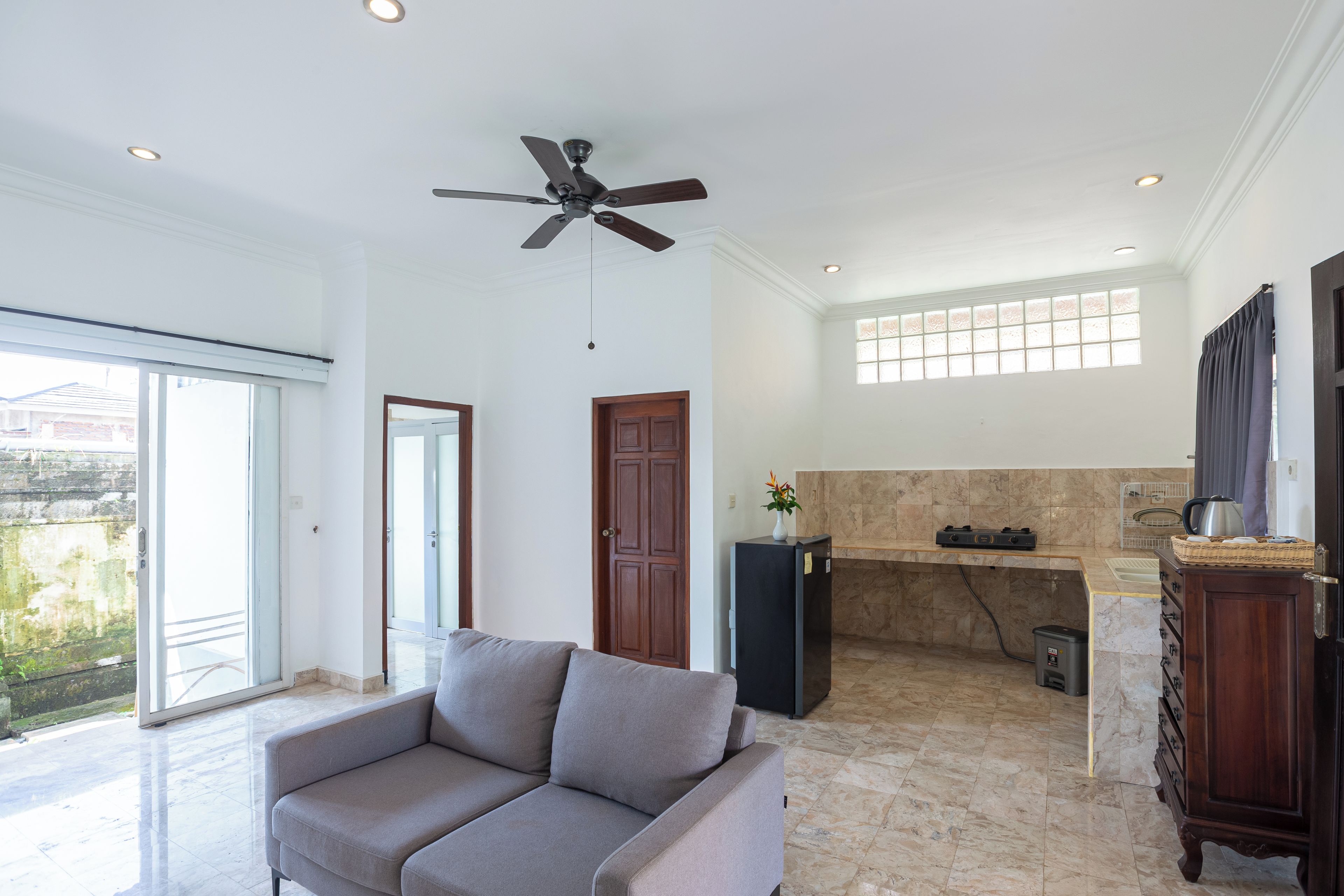 A spacious living area with a ceiling fan, a sofa, a kitchen area with a countertop, and a view through a sliding glass door.