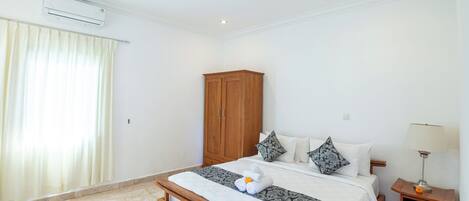 A bedroom with a bed, a wooden wardrobe, a nightstand with a lamp, and a window with curtains.