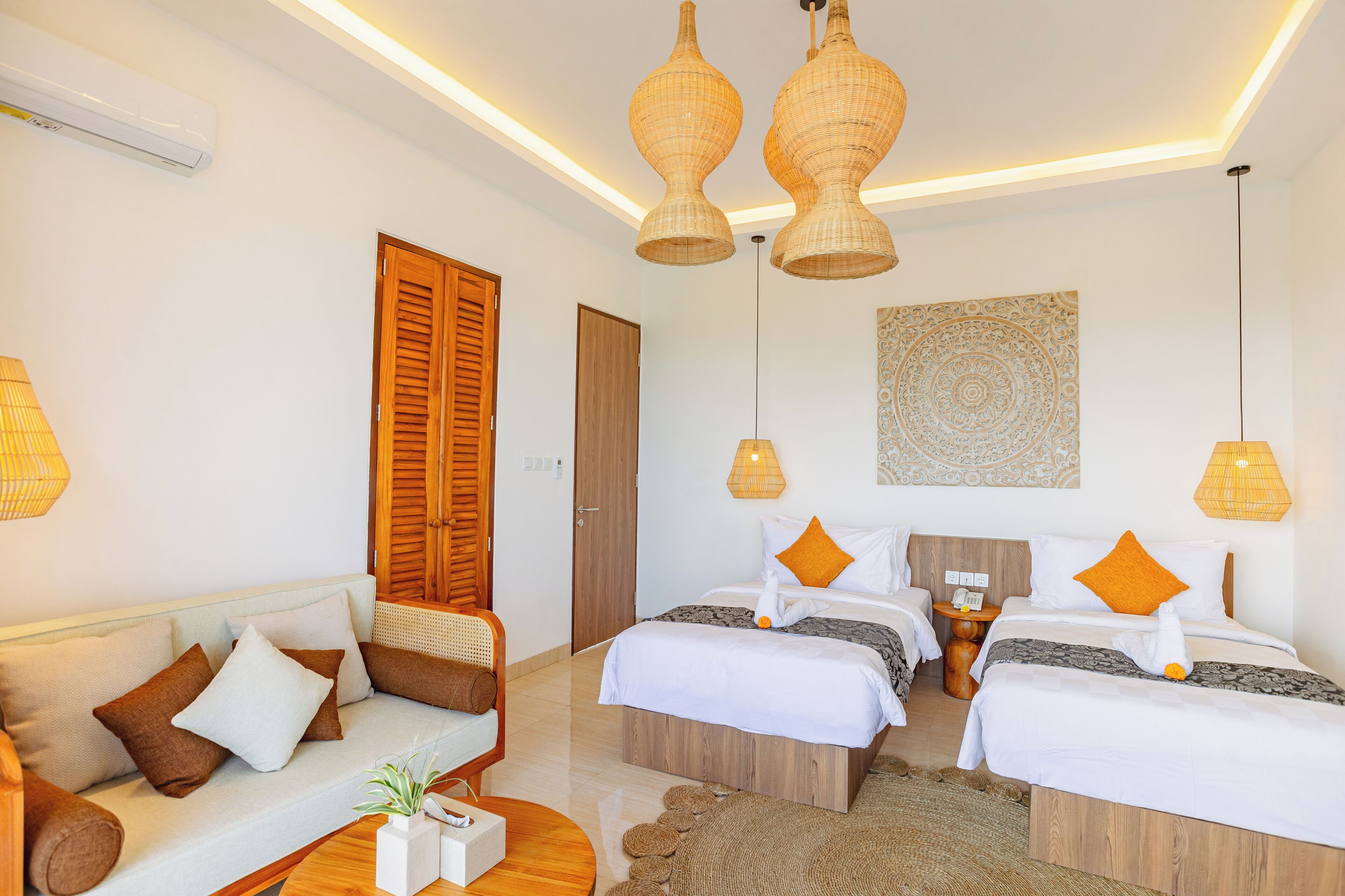 A hotel room with a sofa, two beds, a wall art piece, and a ceiling light fixture.