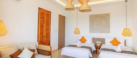 A hotel room with a sofa, two beds, a wall art piece, and a ceiling light fixture.