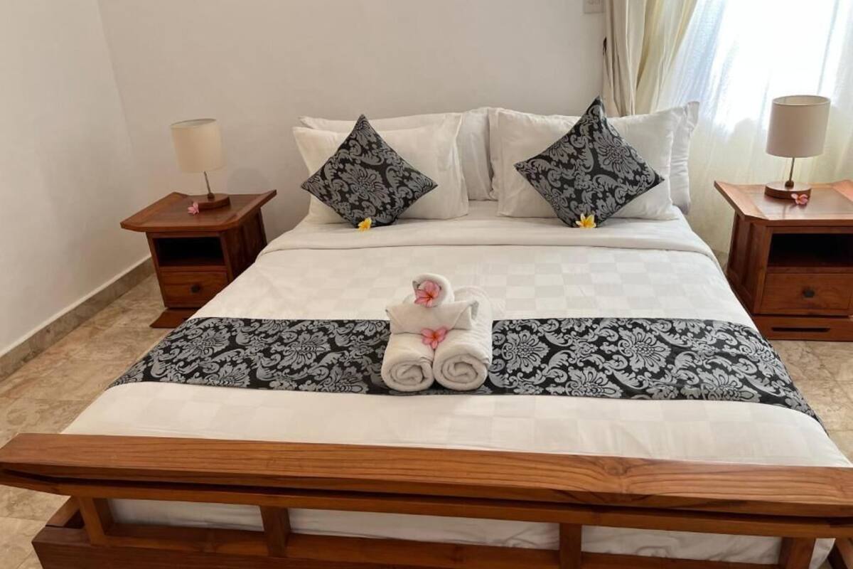 A neatly made bed with a white and black patterned bedspread, two matching pillows, and a pair of rolled towels with a pink flower.