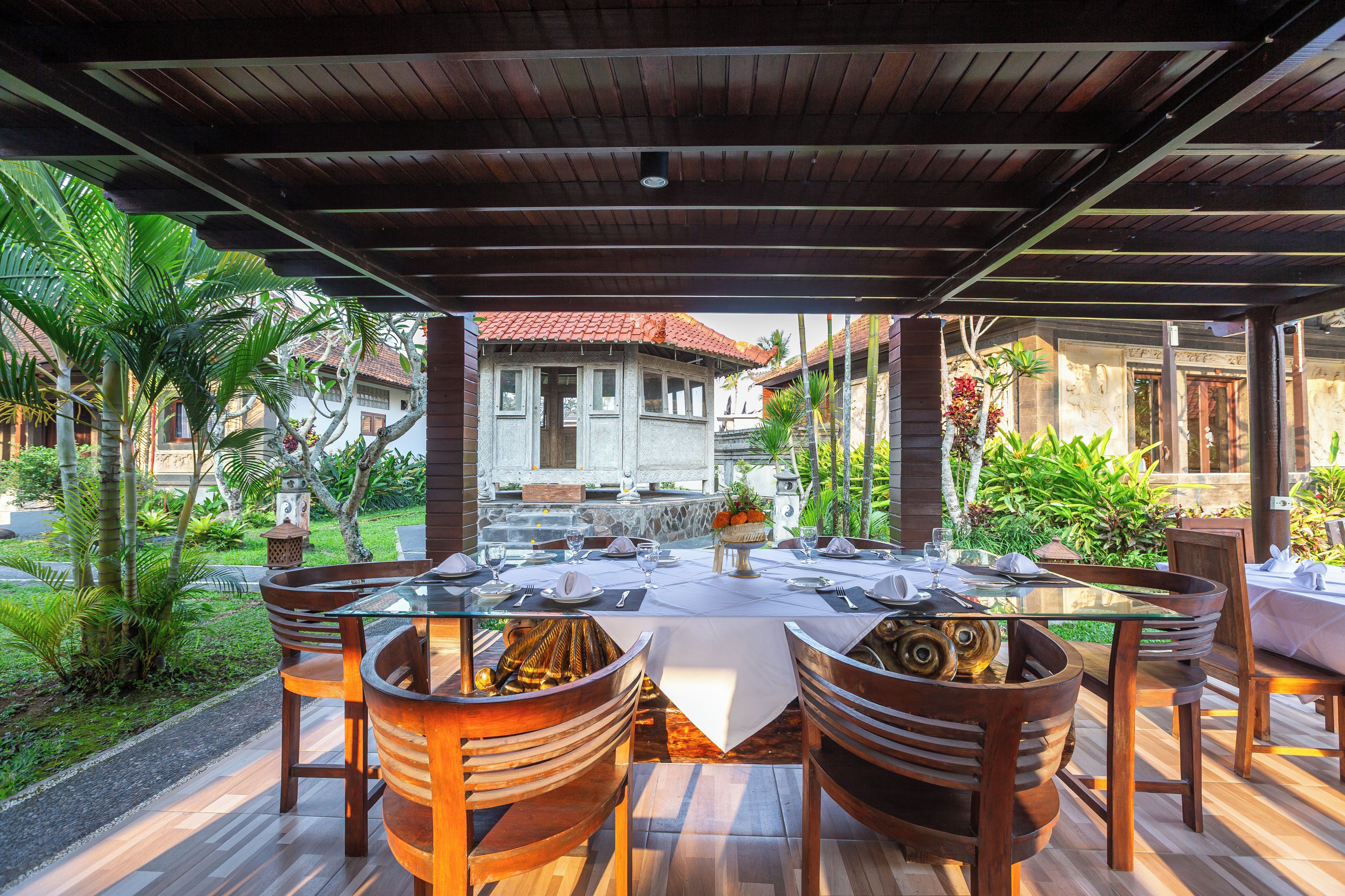 An outdoor dining area with a covered roof, wooden chairs, and a table set for a meal.