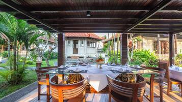 An outdoor dining area with a covered roof, wooden chairs, and a table set for a meal.