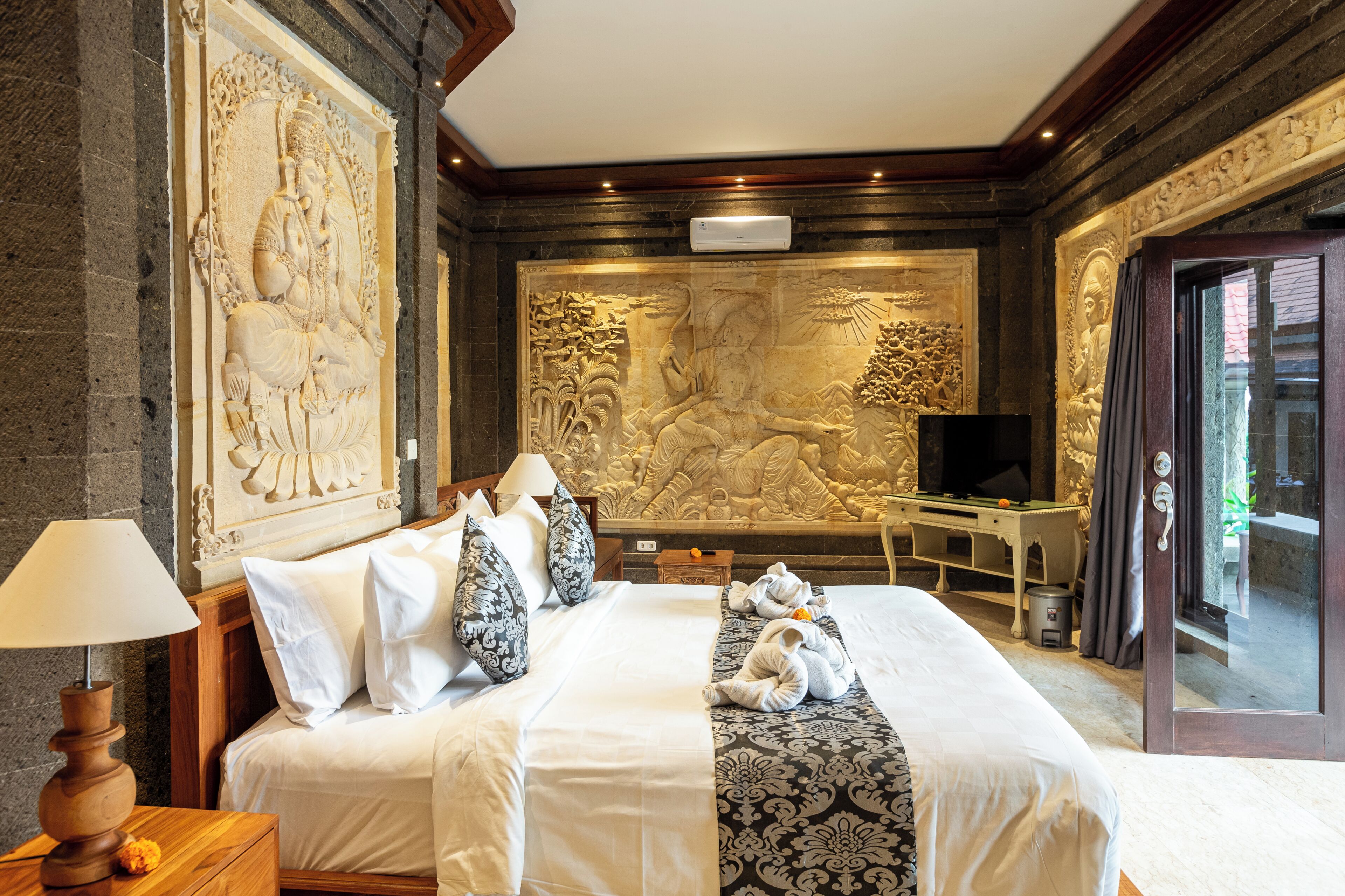 A hotel room with a large bed, a desk, a television, and a stone-carved wall.