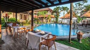 A poolside area with tables and chairs, a pool, and surrounding greenery. - Awatara Villas and Resort Ubud (Kemenuh)