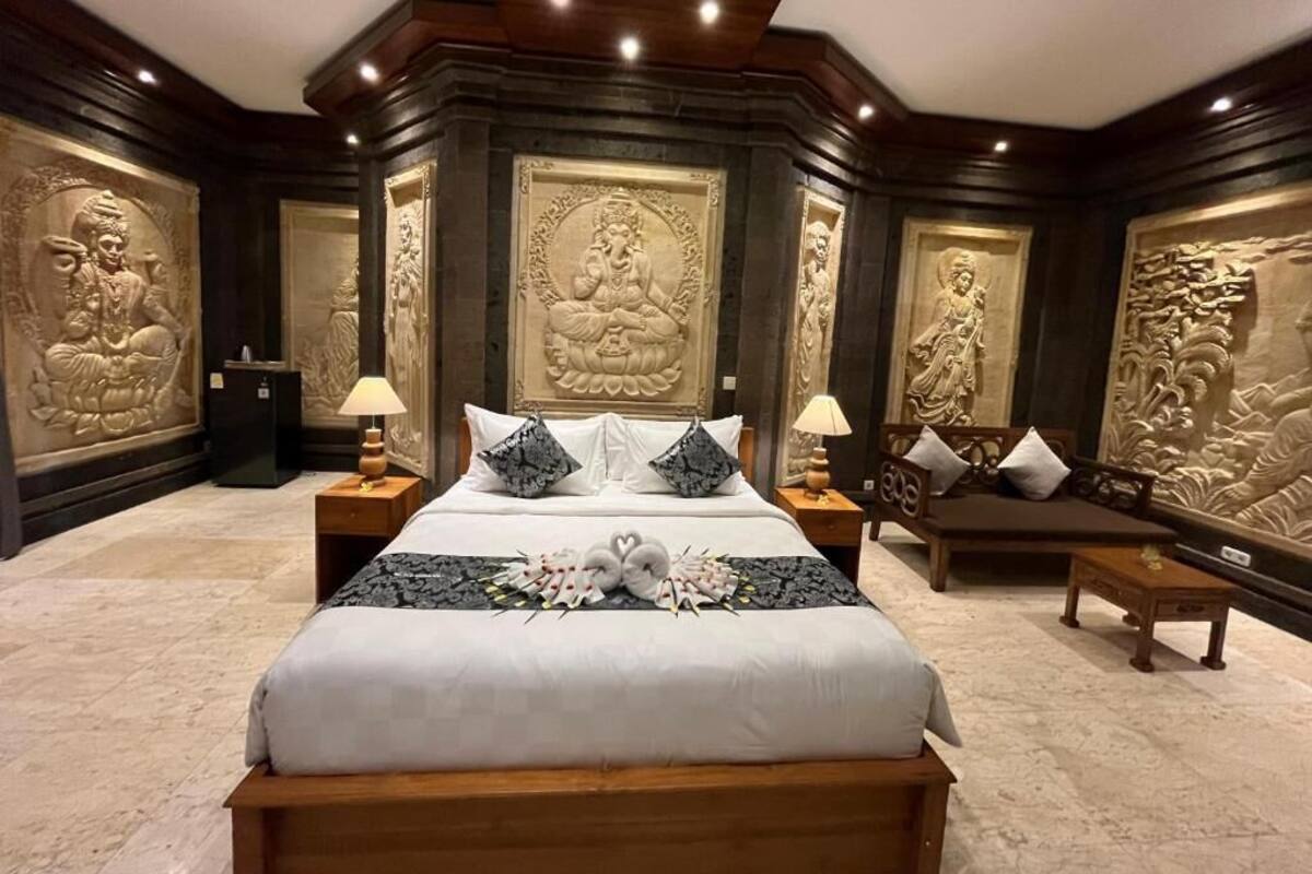 A hotel room with a large bed, two nightstands, a bench, and decorative wall carvings.