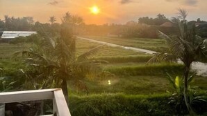 A view of a sunset over a rice field with palm trees and a distant building. - Awatara Villas and Resort Ubud (Kemenuh)