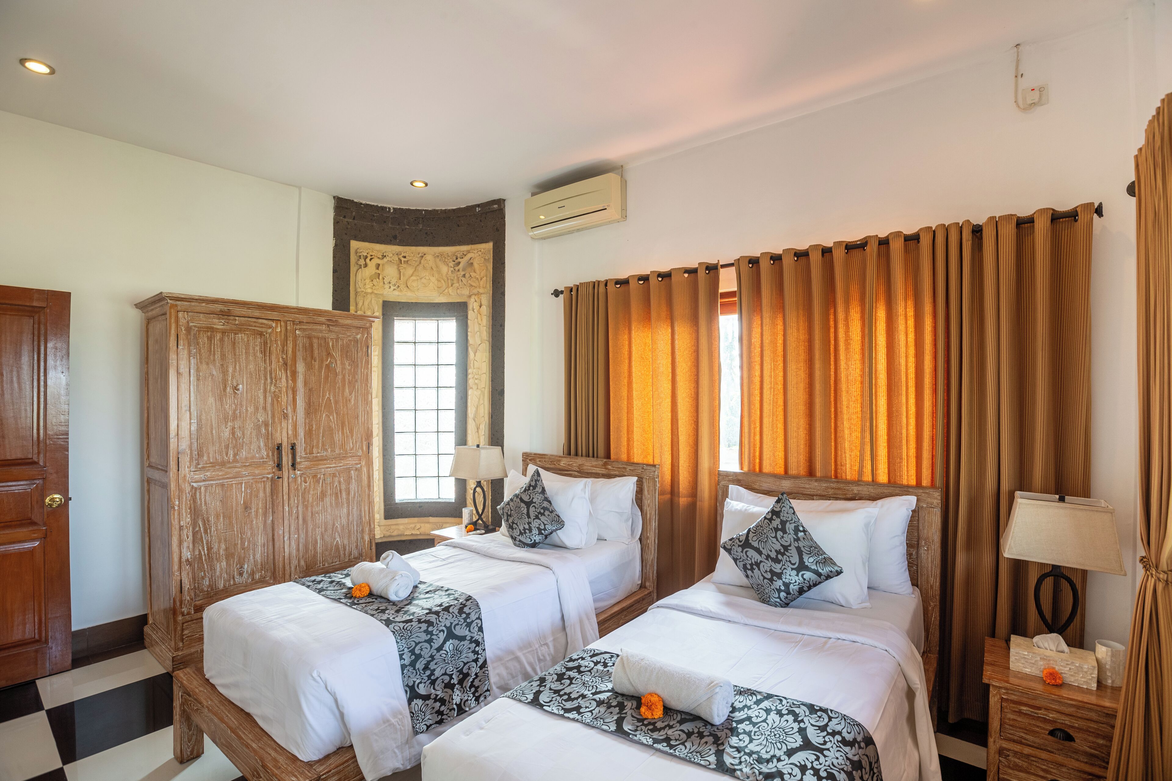 Una habitación de hotel con dos camas, un armario de madera, una ventana con cortinas y un aire acondicionado instalado en la pared.