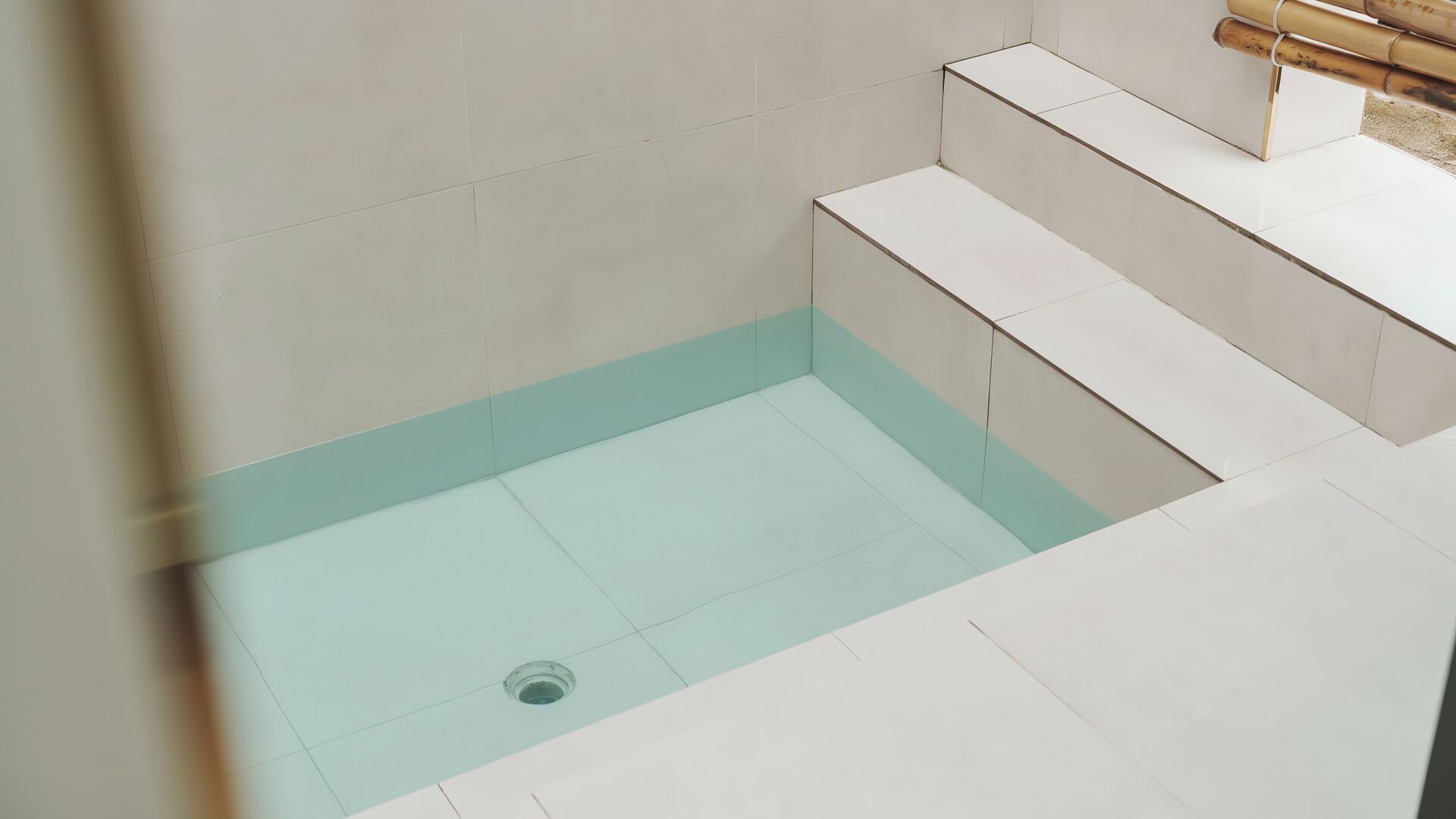 Een moderne badkamer met witte tegels, een glazen douchecabine en een goudkleurige douchekop.