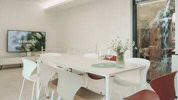 A modern meeting room with a glass table, white and red chairs, a flat-screen TV, and a vase with flowers.
