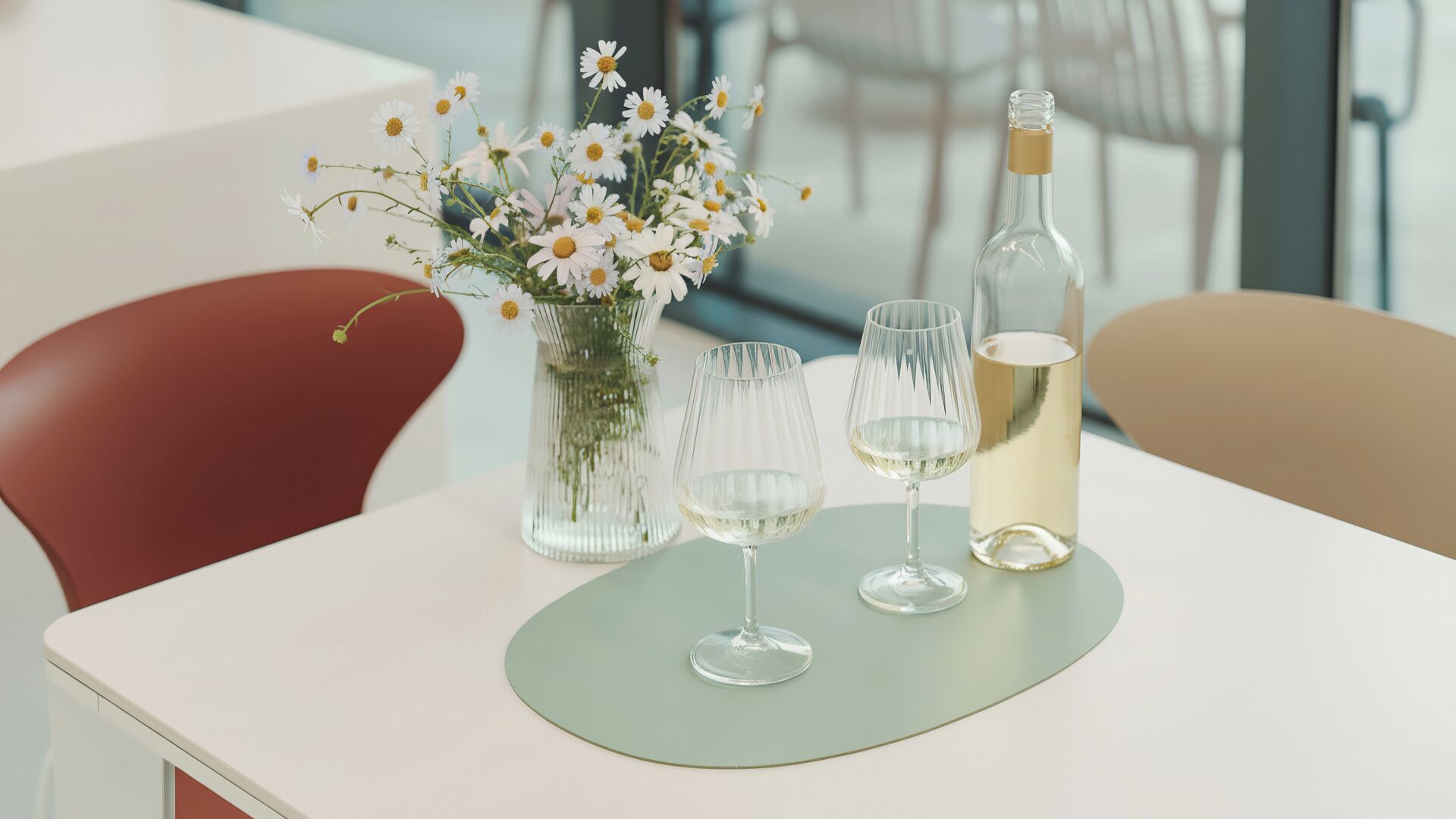 Una mesa con un jarrón de flores, dos copas de vino y una botella.