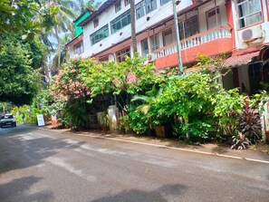 A street with a building featuring a balcony and a lush garden. - Hotel Pete's Hideaway (Panaji)