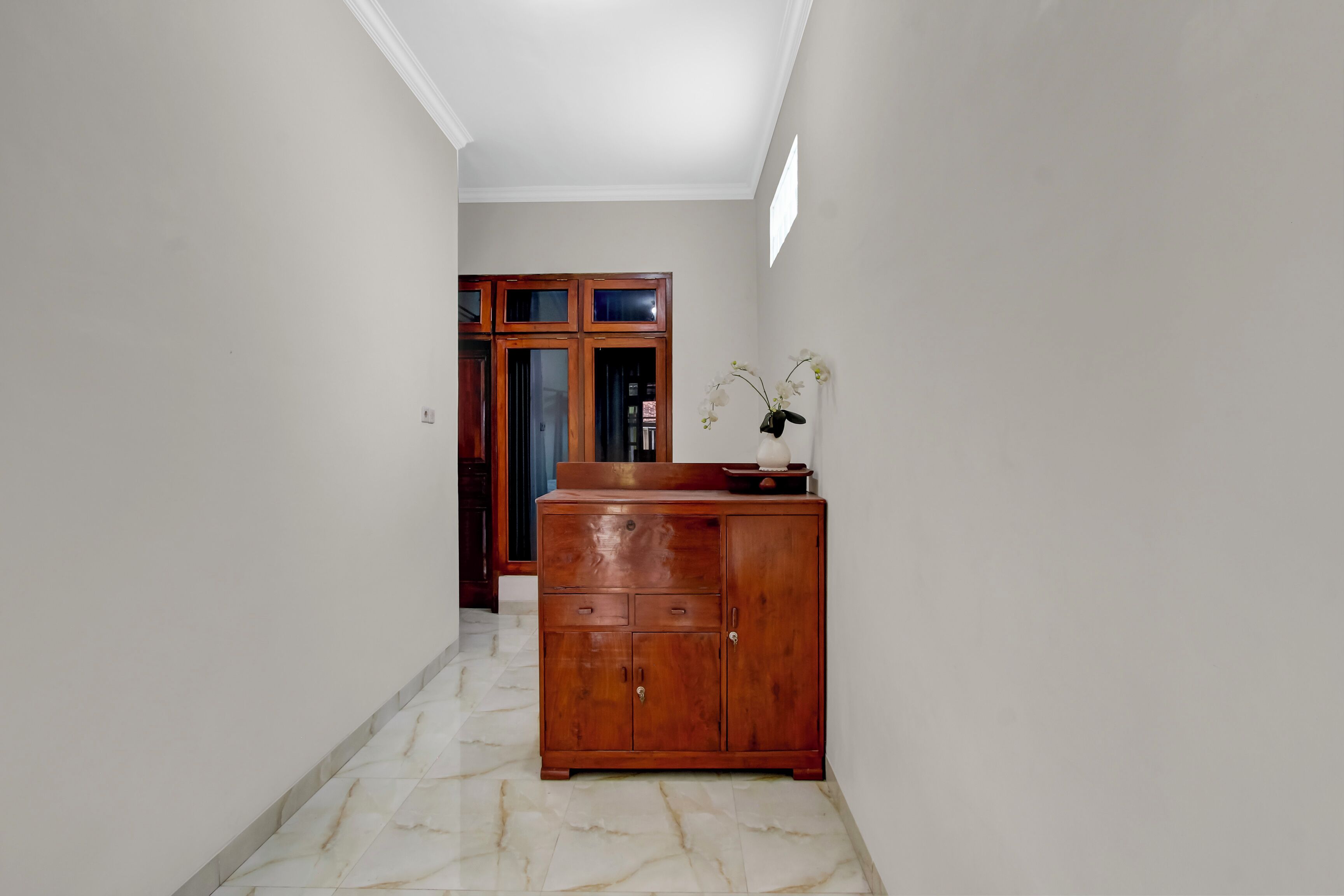 A hallway with a marble floor, a wooden cabinet, and a door in the background.