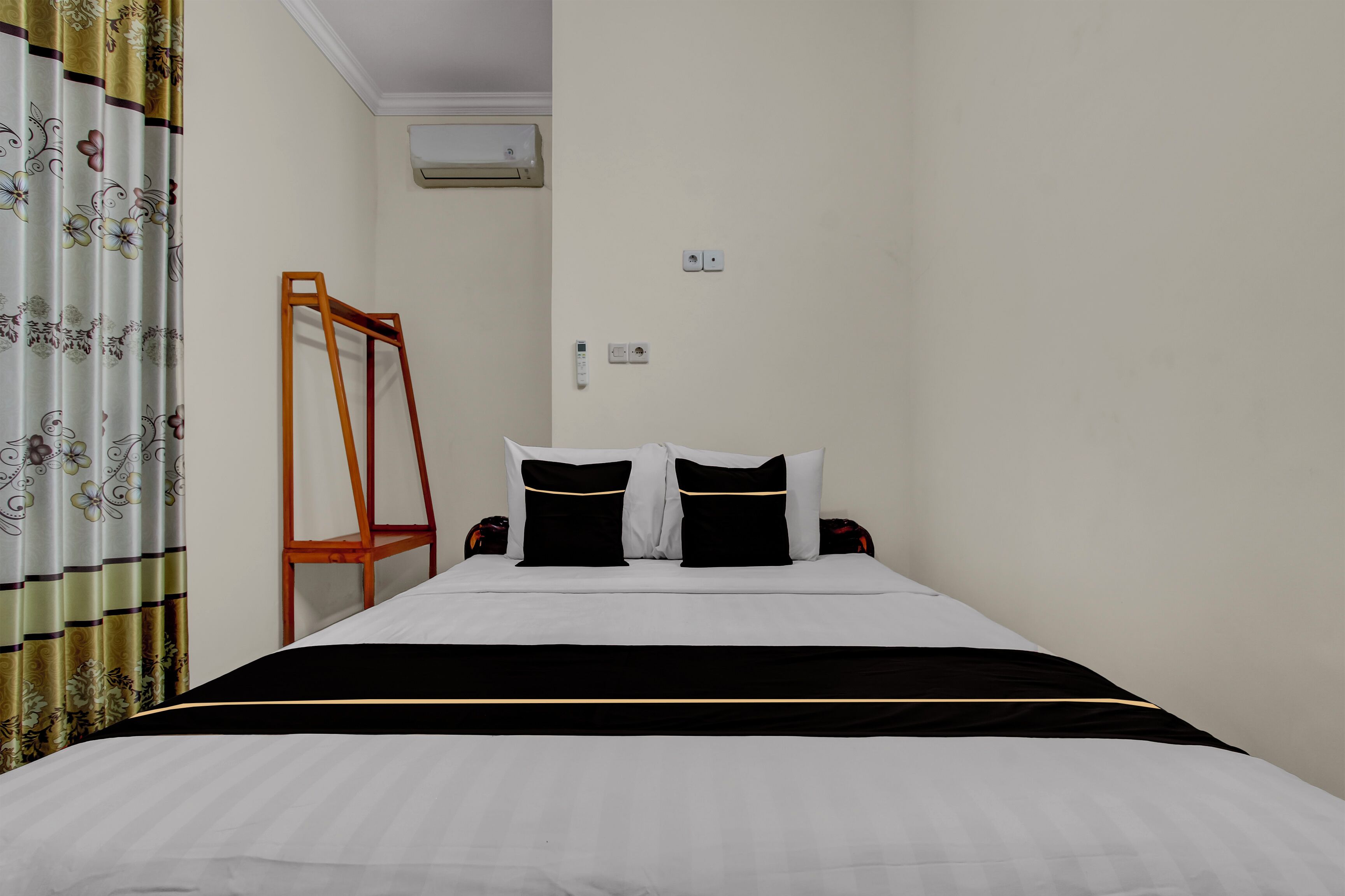 A neatly made bed with a black and white bedspread, a wooden chair, and a floral curtain.