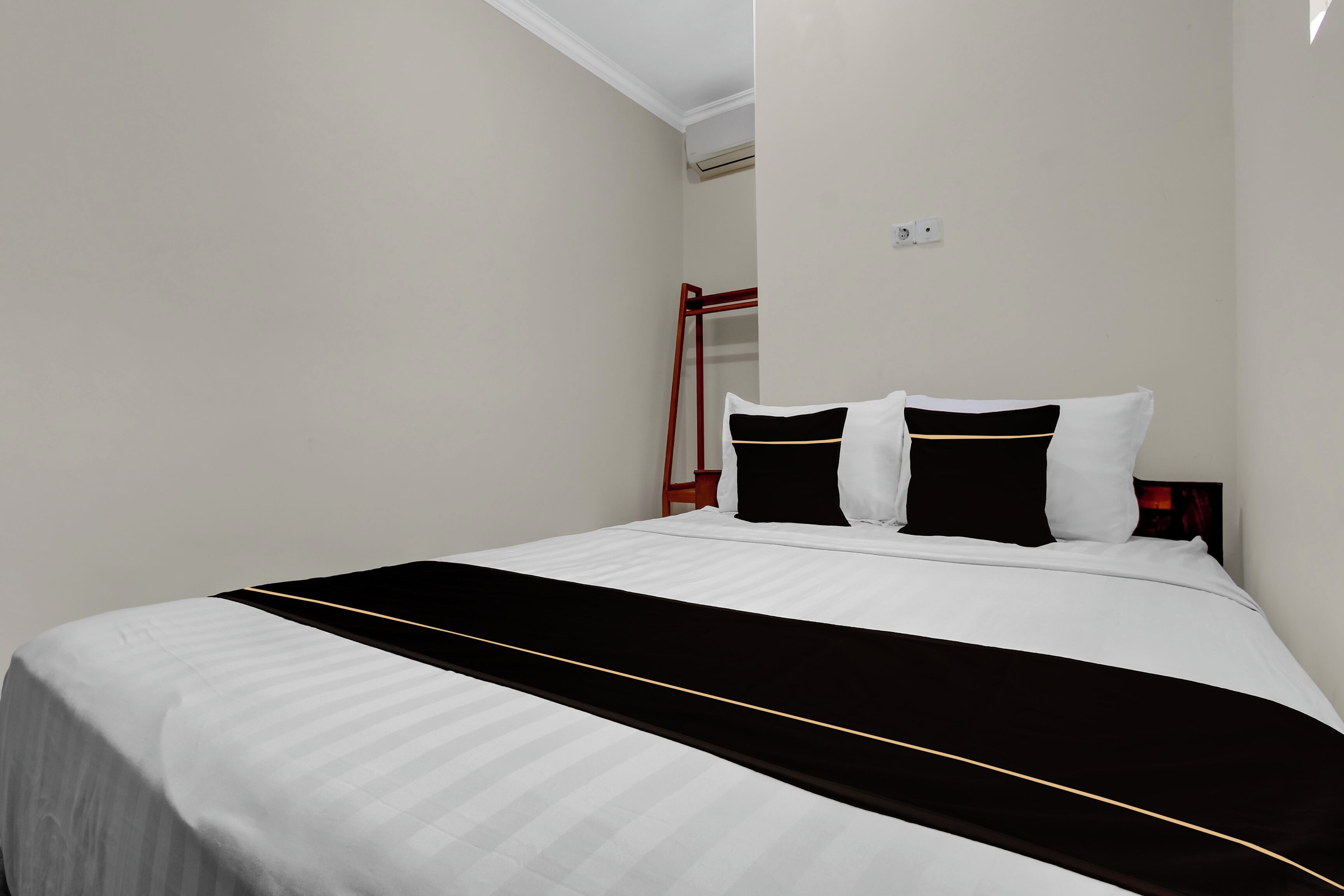 A neatly made bed with white and black bedding, a red metal ladder, and a white wall with an air conditioning unit.