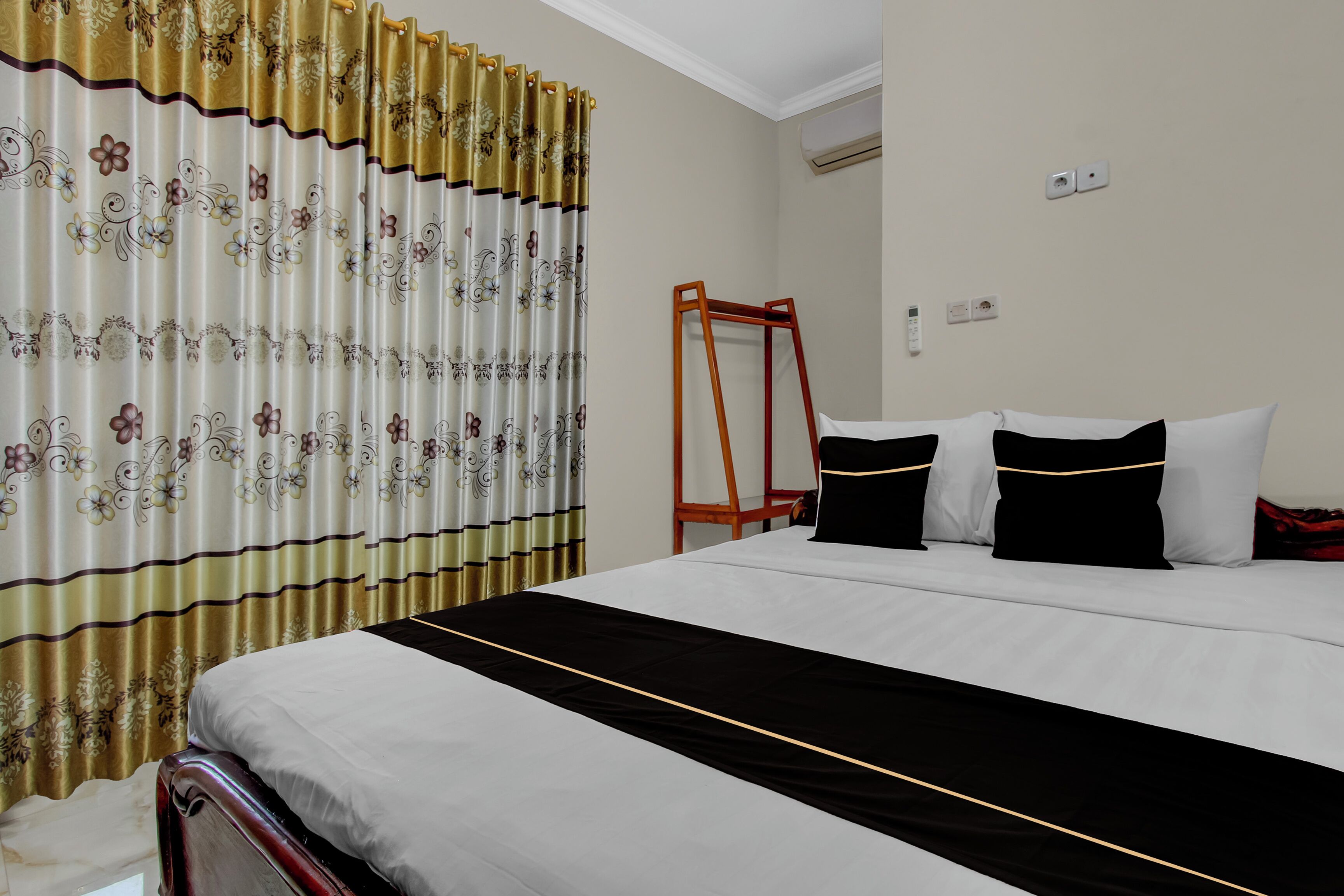 Una habitación de hotel con una cama, cortinas, una escalera de madera y un aire acondicionado instalado en la pared.