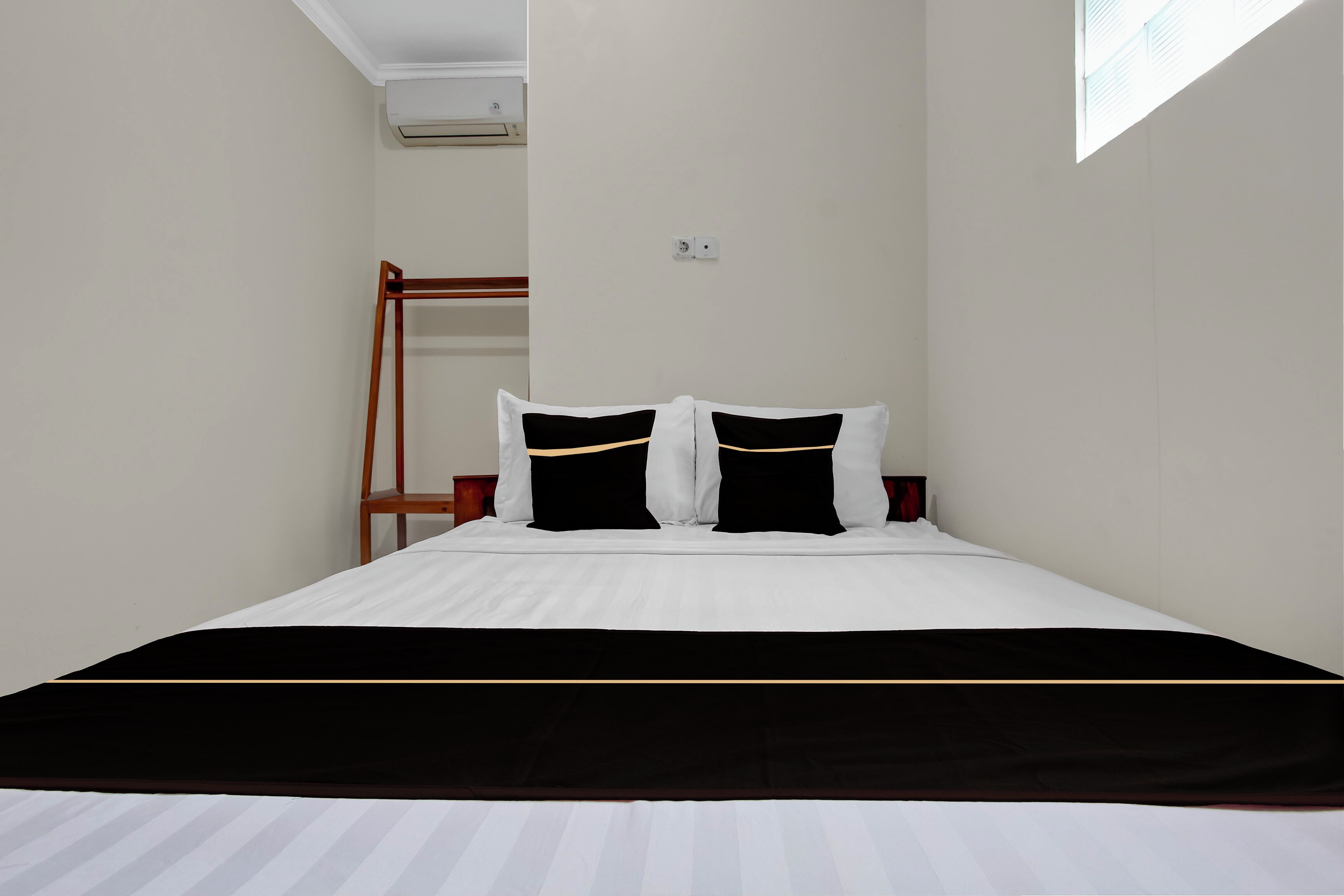 A neatly made bed with white and black bedding, a wooden ladder against the wall, and a small window providing natural light.