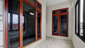 A room with large wooden-framed windows, a tiled floor, and a view of a building with a red roof. - OYO 94920 House Of Elea Minggiran (Yogyakarta)