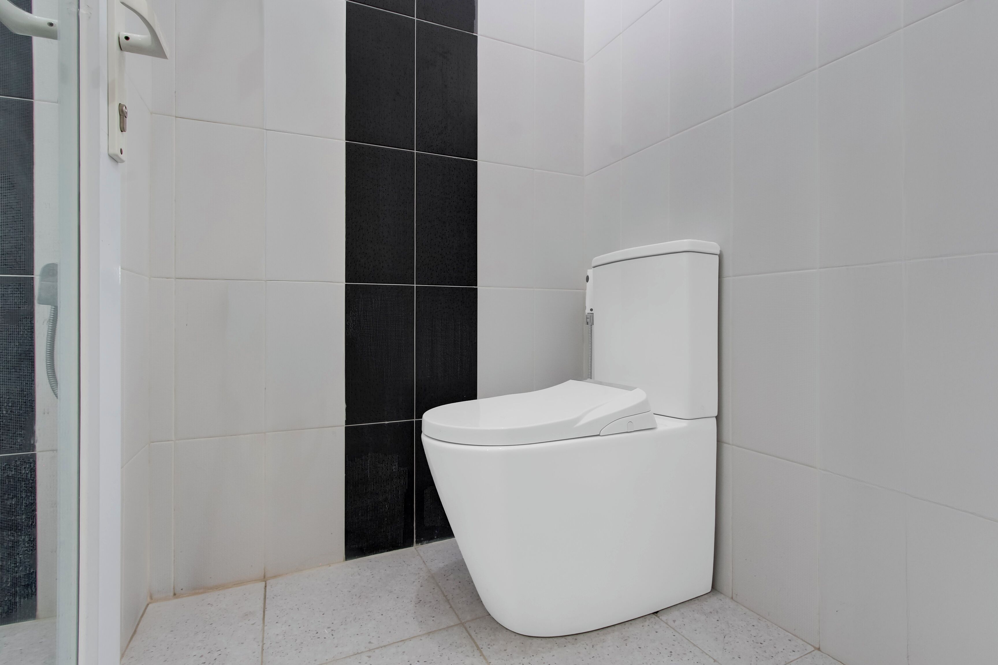 A modern bathroom with white and dark tiles, a white toilet, and a glass shower enclosure.