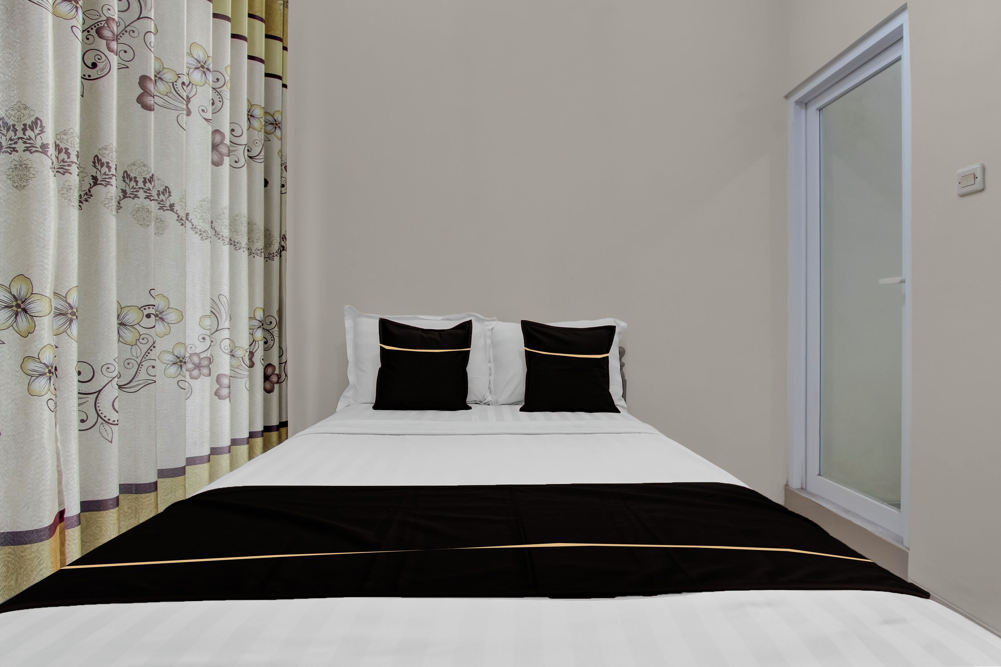 Een hotelkamer met een bed, twee zwarte kussens, een witte dekbedovertrek en bloemen gordijnen.