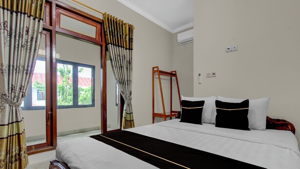A hotel room with a large bed, a wooden headboard, a window with curtains, and a wooden ladder against the wall. - OYO 94920 House Of Elea Minggiran (Yogyakarta)