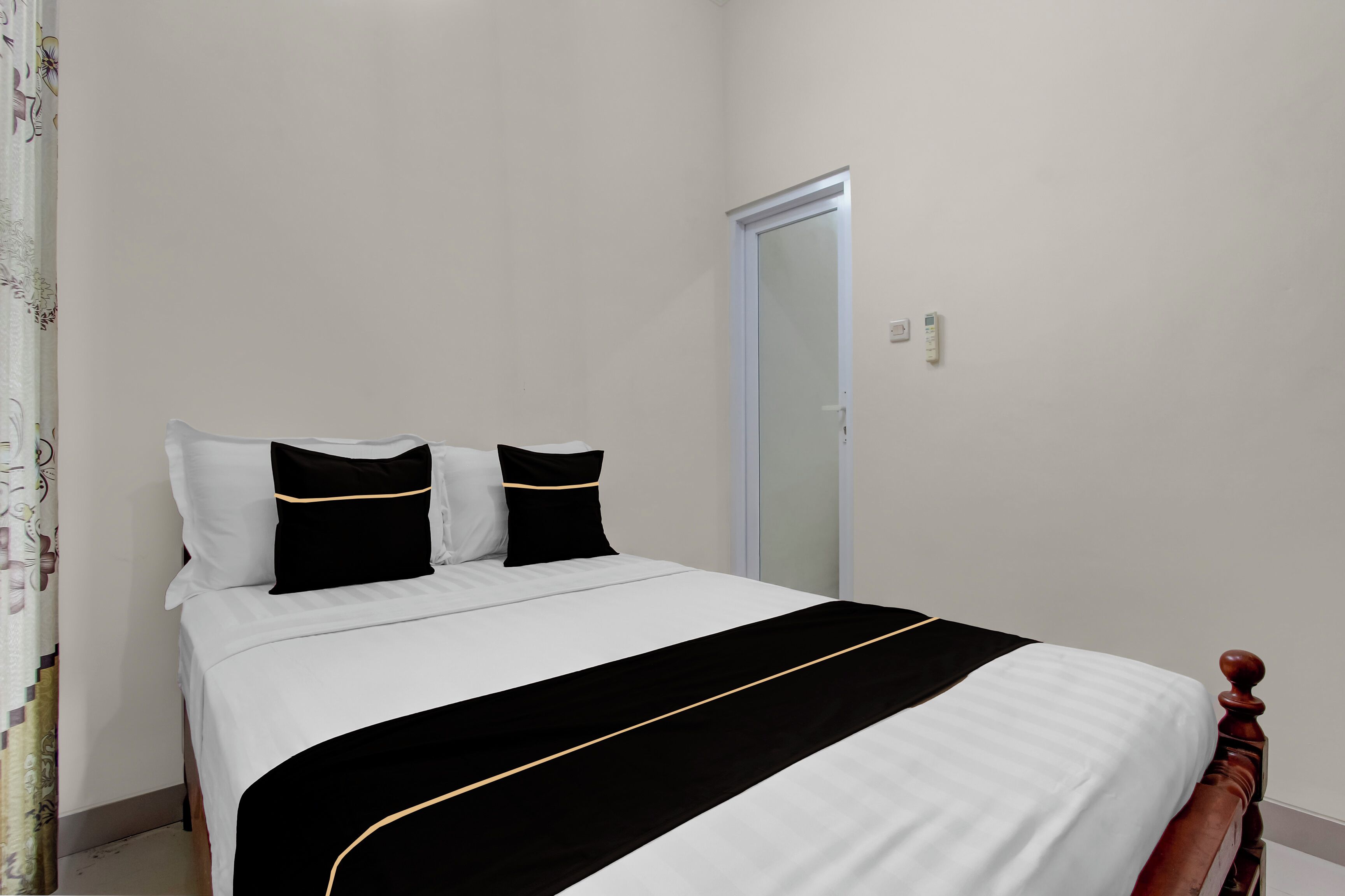 A neatly made bed with white and black bedding, a wooden headboard, and a door to the right.